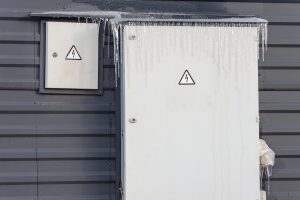 Frozen and covered with icicles fuse box installed outside on the wall of a building